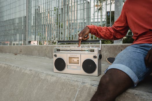 Close-up of a young man's hand operating a retro boombox in a city setting. Nostalgic urban vibes.