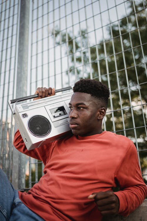 Free Young pensive African American male with Afro haircut listening to audio from old portable cassette recorder while looking away on street Stock Photo
