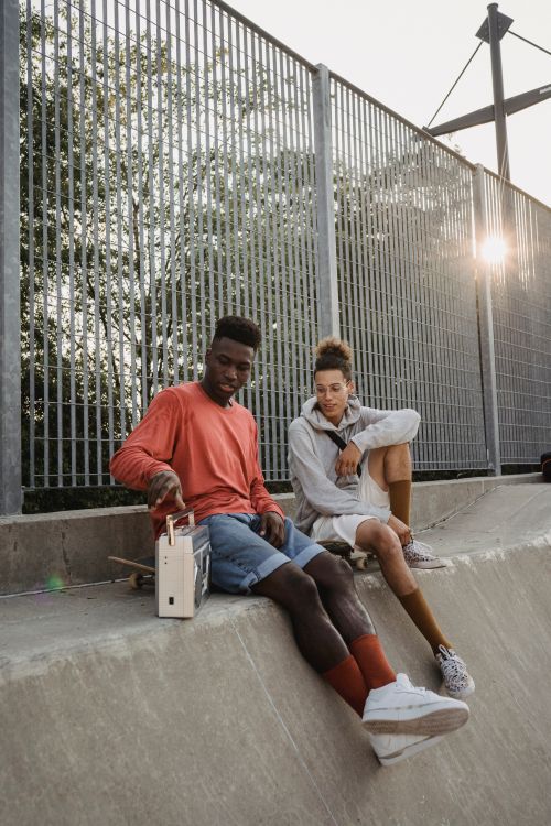 Free Young multiethnic sportsmen listening to song on retro cassette recorder while sitting on platform in skate park Stock Photo