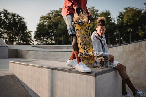 Crop anonymous ethnic sportsman with skateboard standing on platform near pondering male partner in urban skate park