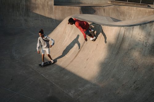 Free From above of unrecognizable multiracial sportsmen balancing on skateboards on skate ramp in sunlight Stock Photo