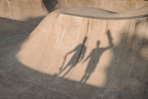Free From above of silhouettes of faceless sportsmen with skateboards standing on skate ramp in soft sunlight Stock Photo