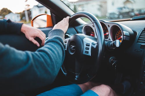 Free Crop anonymous male in casual outfit touching steering wheel and riding contemporary automobile Stock Photo