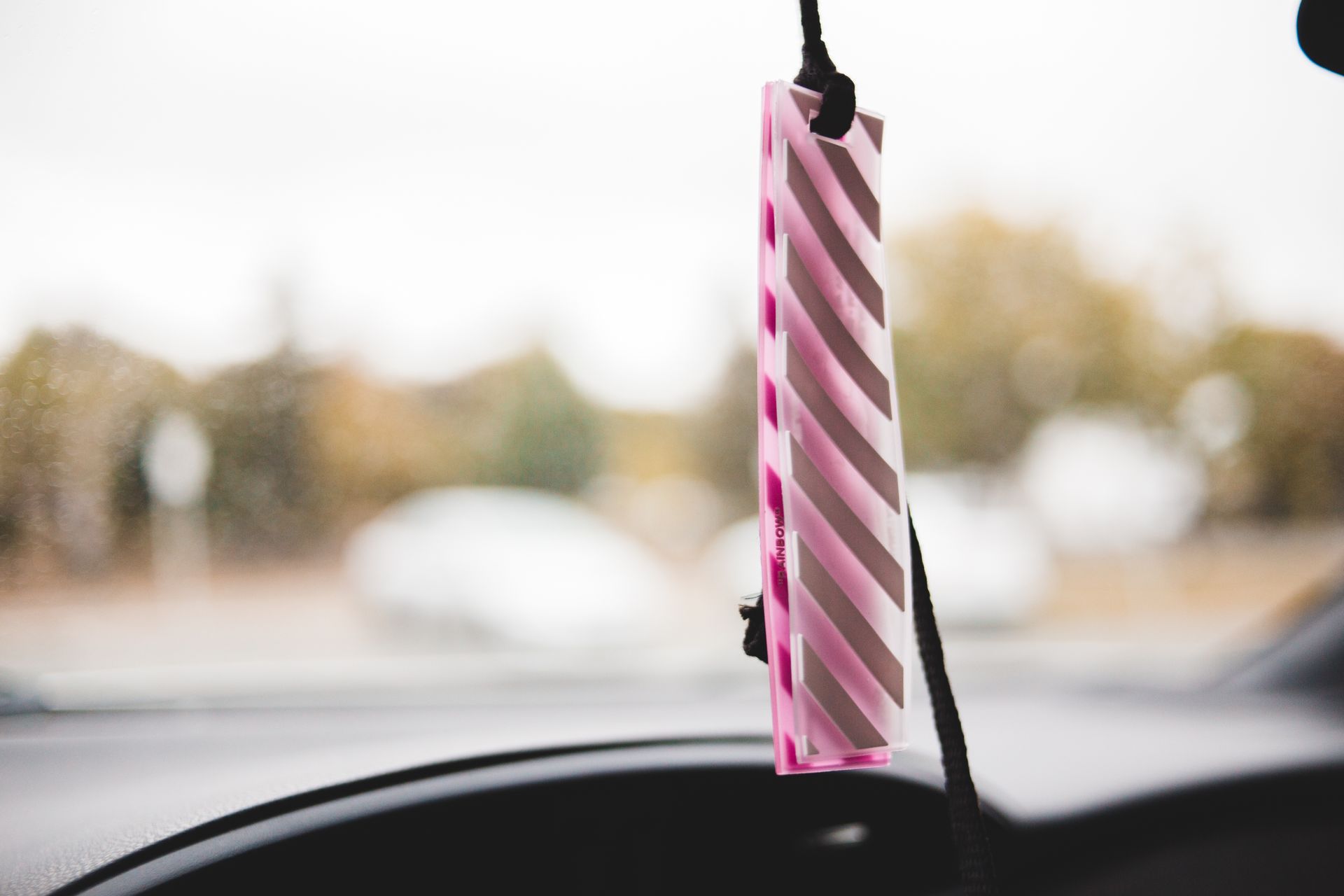 Stylish pink striped air freshener hanging in a car interior with blurred background.