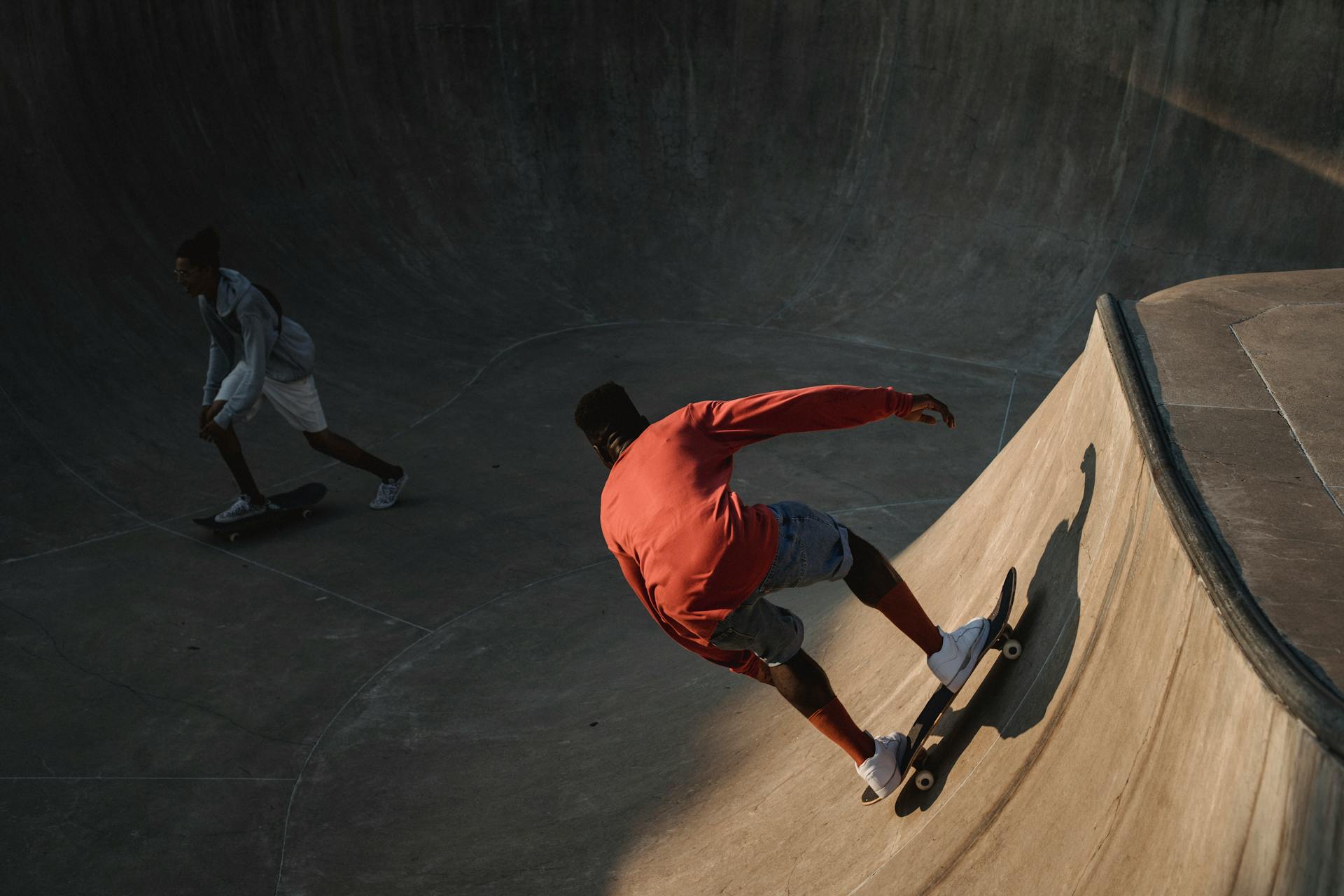 Unrecognizable ethnic friends skateboarding on skate ramp in evening