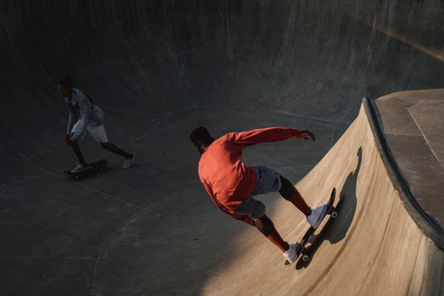 Free Anonymous black sportsman balancing on skateboard near partner while practicing extreme sport on platform in soft sunlight Stock Photo
