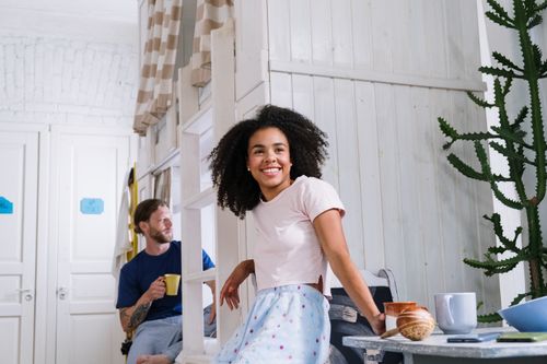 Free Joyful couple enjoying coffee together in a bright, cozy dorm room with a modern touch. Stock Photo