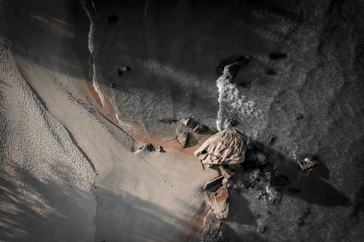 From above of transparent water washing coast with rocks and shadow in dark