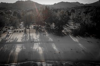 Drone view of peaceful sandy beach with cars on parking and trees against picturesque rocky mountains in morning
