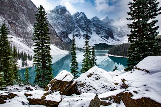 Majestic winter landscape of Moraine Lake surrounded by snow-covered mountains and pine trees.