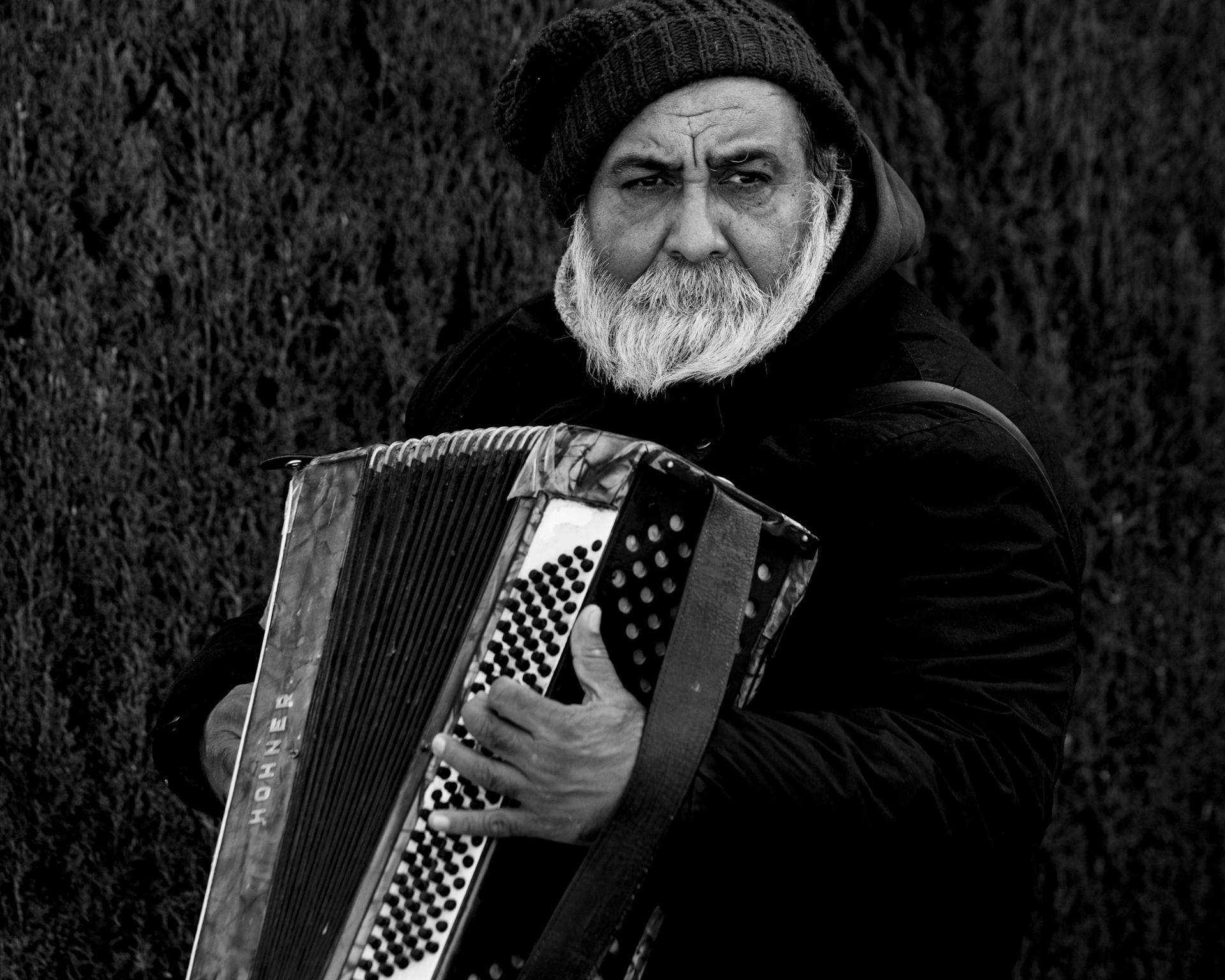 Black and white portrait of an elderly man playing accordion outdoors.