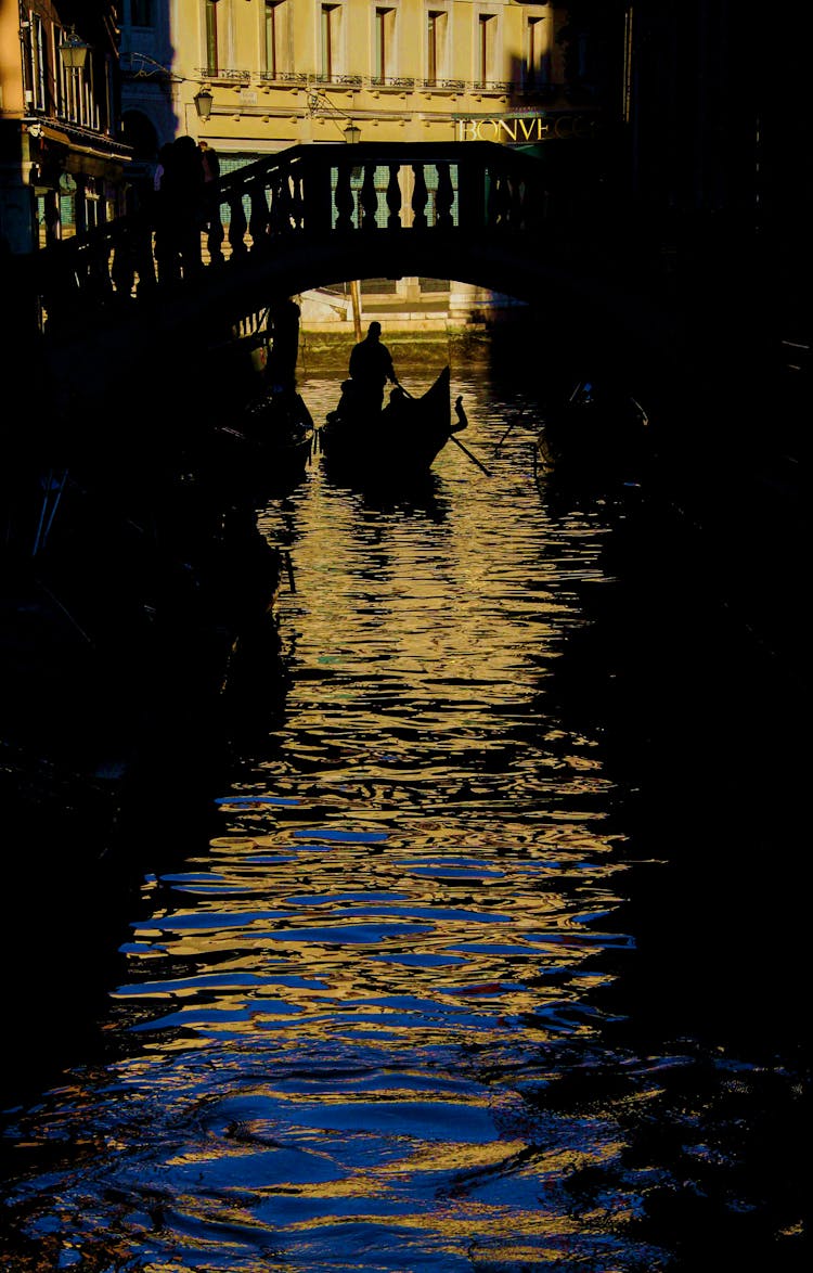 Silhouette Of A Person Sailing In A Gondola Under A Bridge 