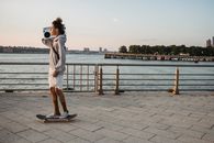 滑板手穿着休闲服装，在河边的长廊旁欣赏音乐