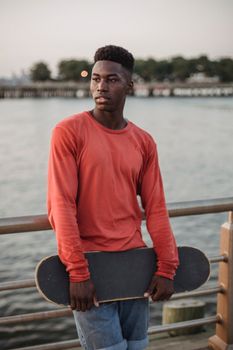 一位身着休闲服的年轻非裔美国男性体贴地站在路堤上，靠近栅栏，望向远方