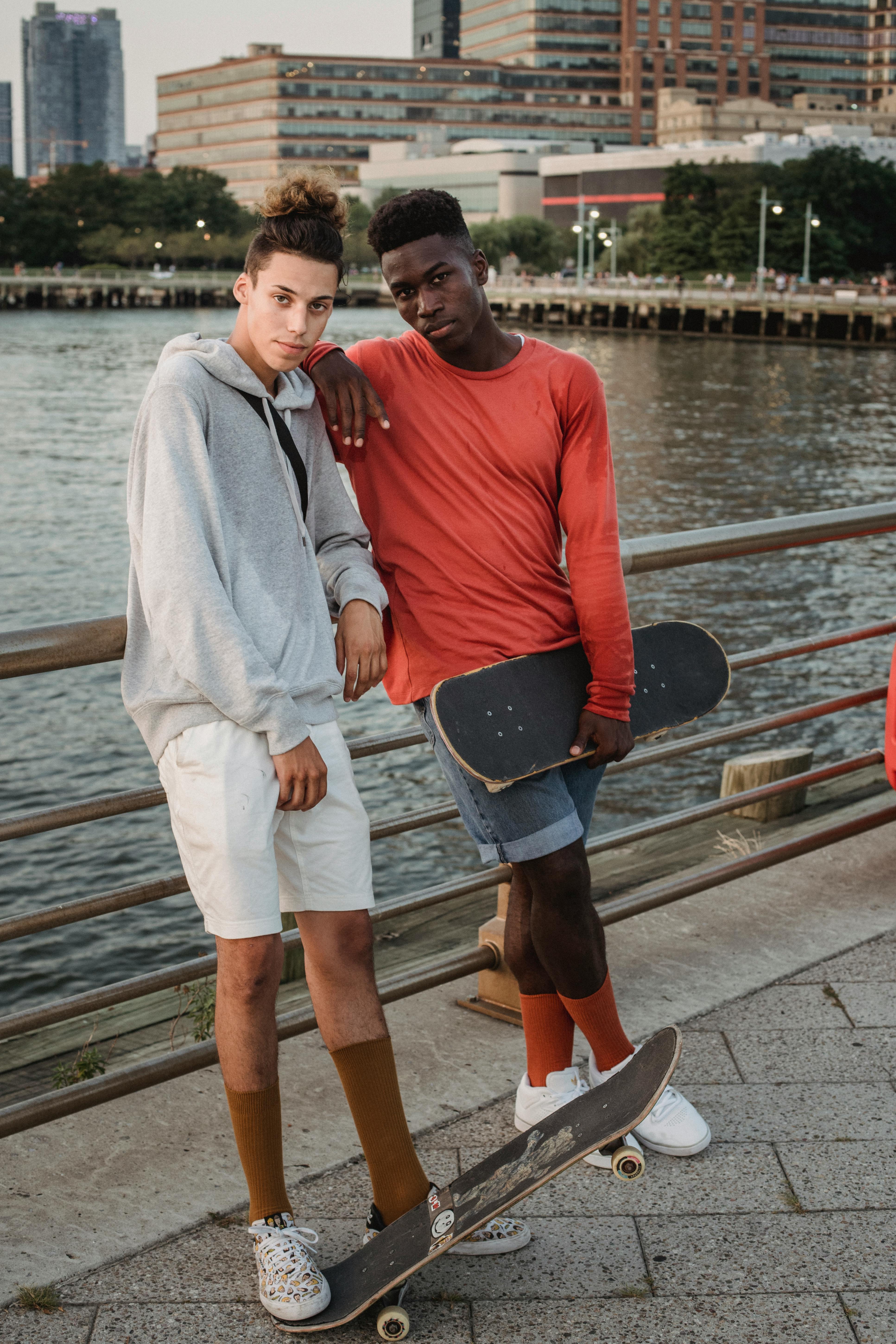 一位神情严肃的年轻男滑冰运动员，带着滑板站在海滨，看着镜头