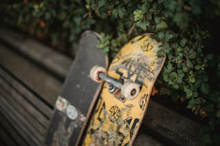 Shabby skateboards with rubber wheels placed on wooden bench in park near green fence
