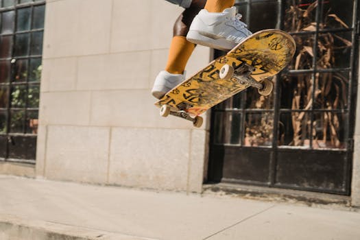 Crop black male skater jumping on skateboard while doing stunt on pavement near building