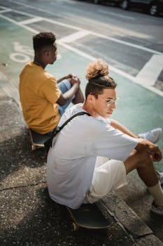 Young diverse male skaters in casual clothes sitting on skateboards on pavement while resting in sunny day