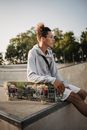一个阳光明媚的日子里，一位年轻自信的男性滑板运动员在滑板公园的混凝土坡道上休息，这是他的侧视图