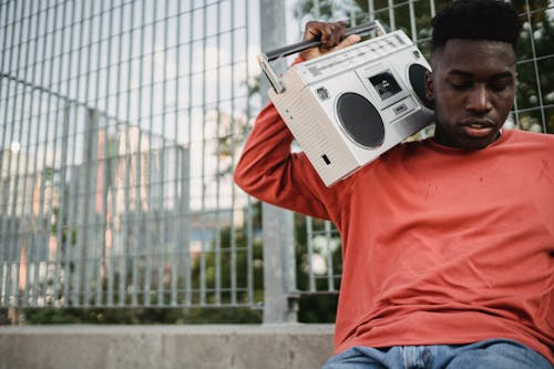 Free Young African American male in casual outfit sitting in park with boombox and listening to music Stock Photo
