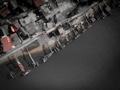 Drone view of coastal village with small houses and parked cars placed near berth with moored boats on calm sea at daytime