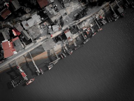 Drone view of coastal village with small houses and parked cars placed near berth with moored boats on calm sea at daytime
