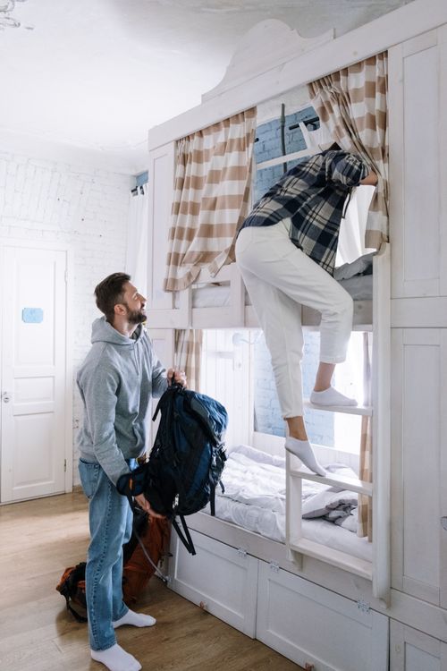 Free Couple packing bags in a bright, cozy hostel dormitory room with bunk beds and wooden floor. Stock Photo