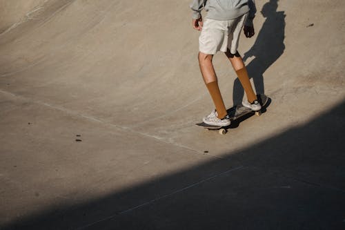 Free Crop anonymous male skater wearing white shorts riding skateboard on asphalt ramp in skate park on summer sunny day Stock Photo