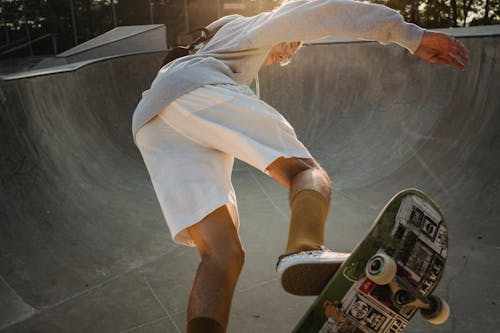 From below of young confident guy in activewear performing ollie stunt on skateboard on concrete ramp in skate park on summer sunny day