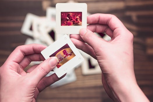 Close-up of hands holding vintage photo slides with faded images on a wooden table background.