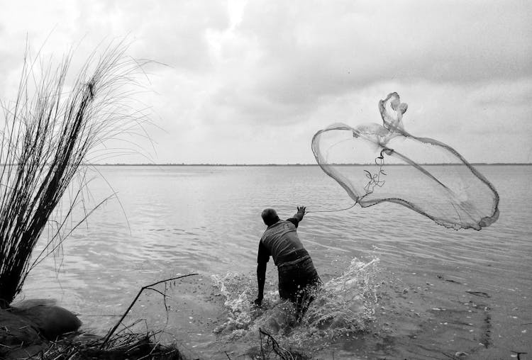 Man Throwing A Fishing Net On The River