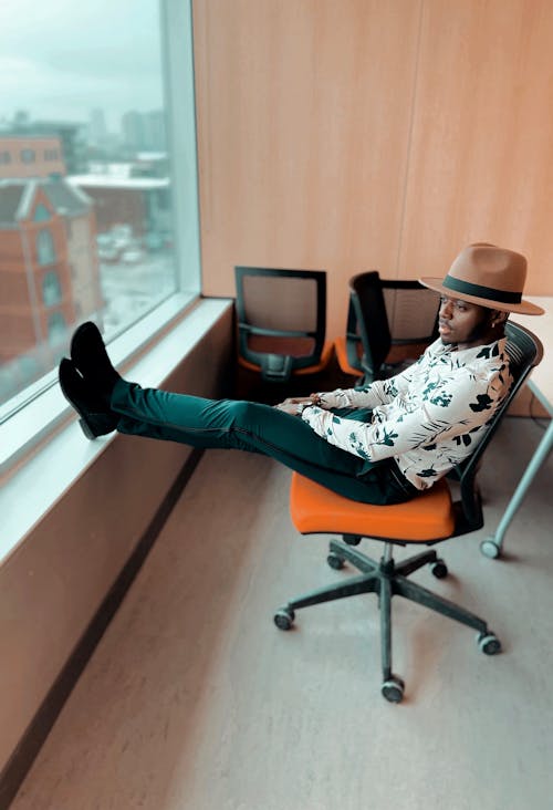 Stylish black man sitting on chair with legs on windowsill