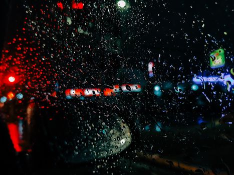 Vibrant city lights blurred through rain-soaked car window, creating an atmospheric night scene.