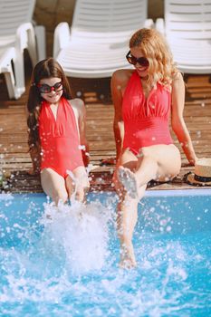 Mother and daughter in red swimsuits enjoying a sunny day by the pool.