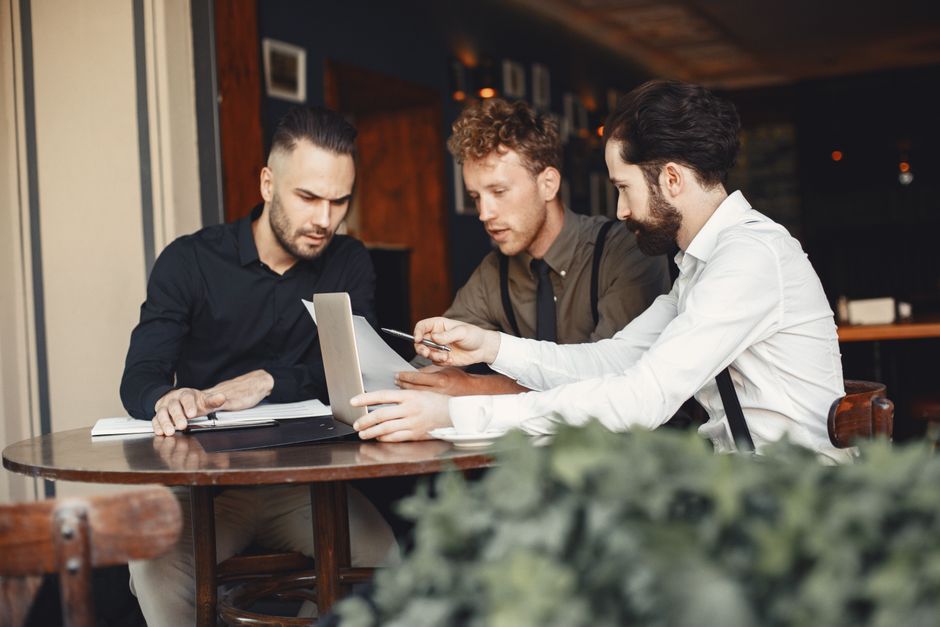 Three young men collaborating in a cozy cafe setting, focused on a laptop. Three young men collaborating in a cozy cafe setting, focused on a laptop.