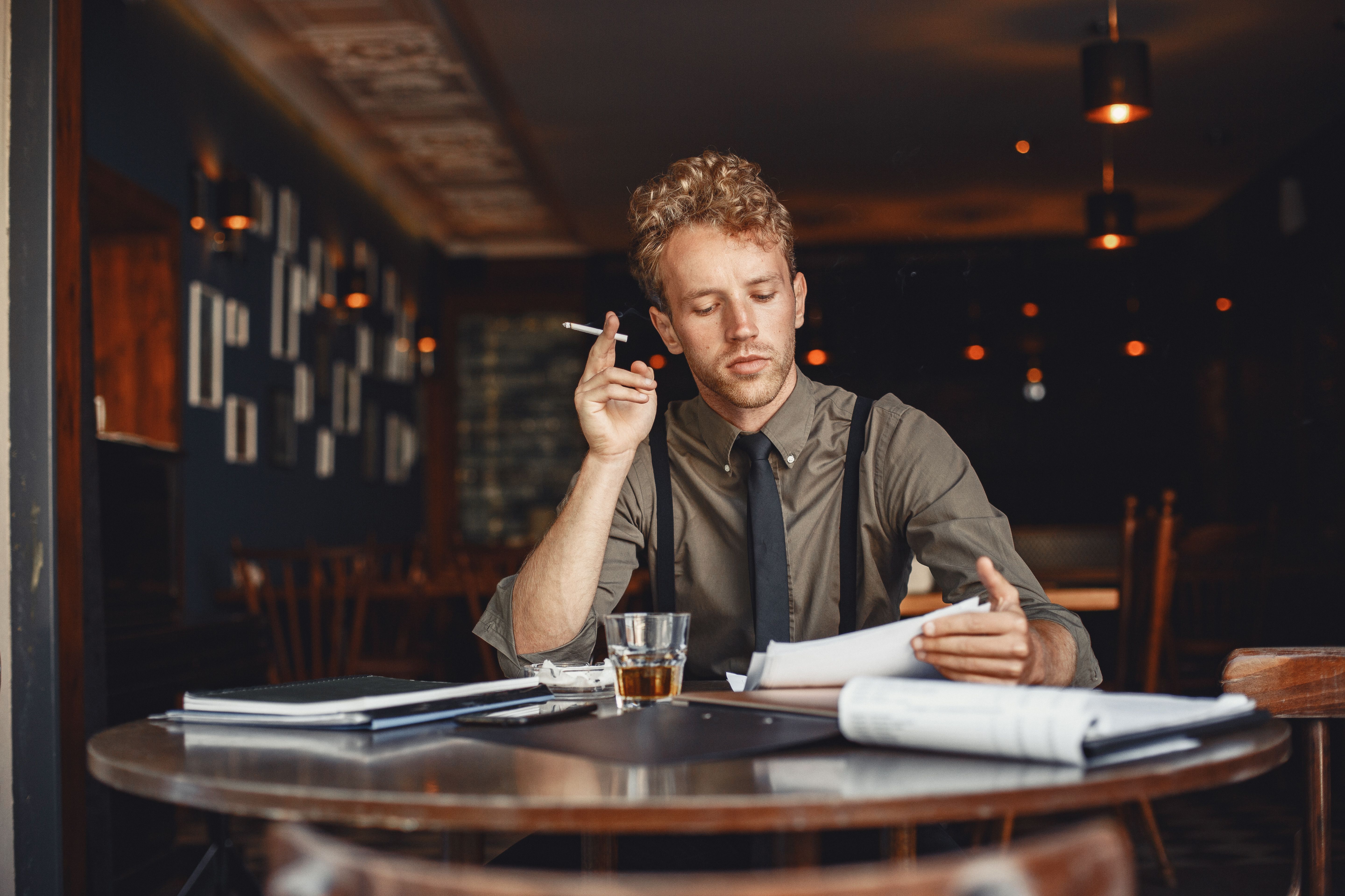 Thoughtful man reviewing documents in a cozy cafe, smoking a cigarette.