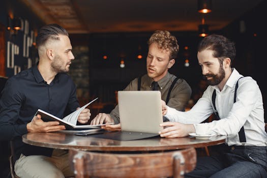 Three professionals engaged in a business meeting in a stylish cafe, discussing work over a laptop.