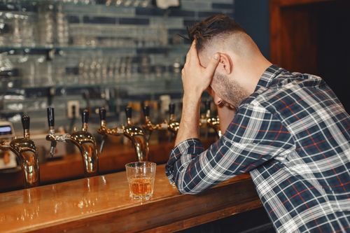 Free Man sitting at a bar counter with a glass of whiskey, appearing contemplative. Stock Photo