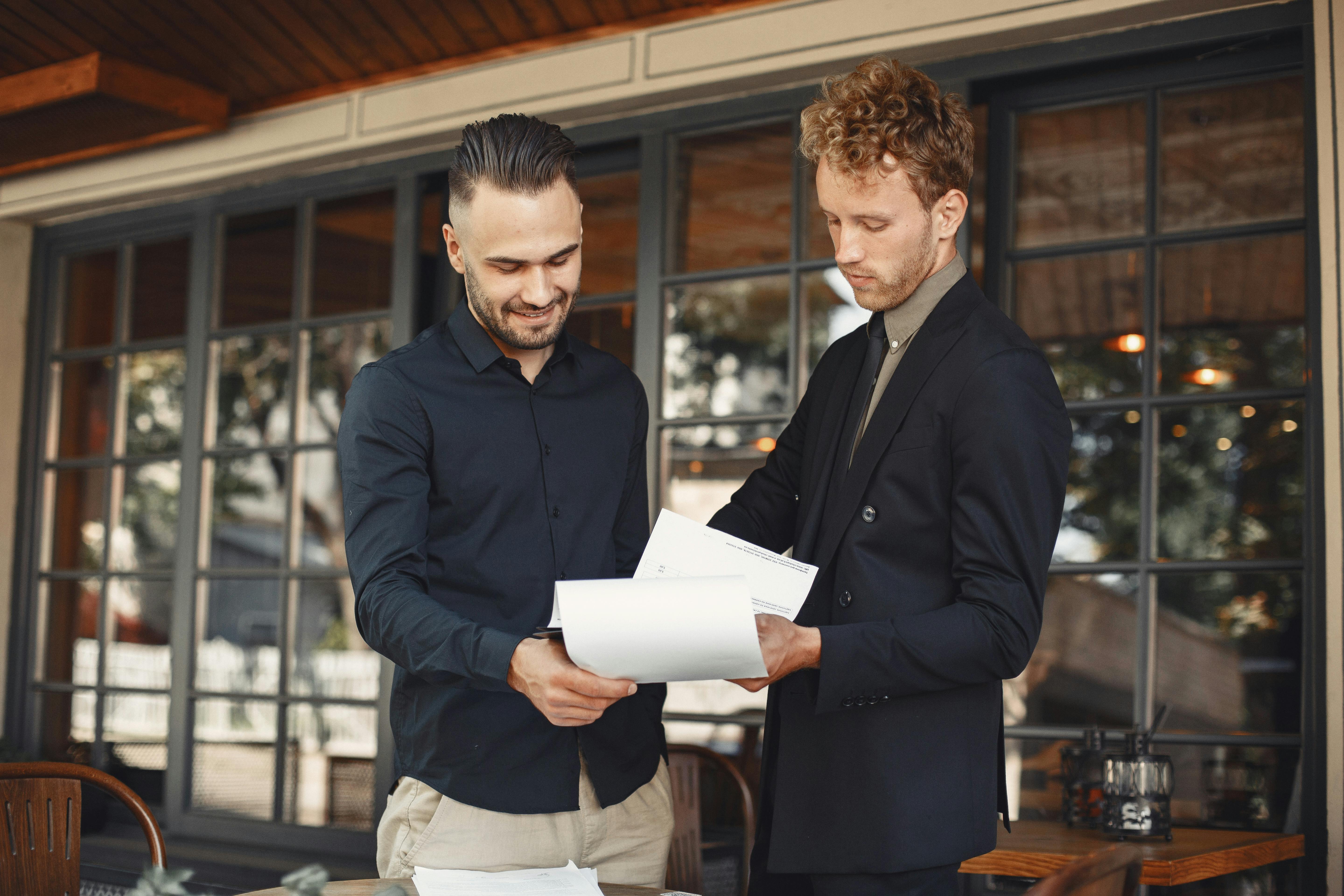 Two businessmen discussing documents at a professional meeting outdoors.