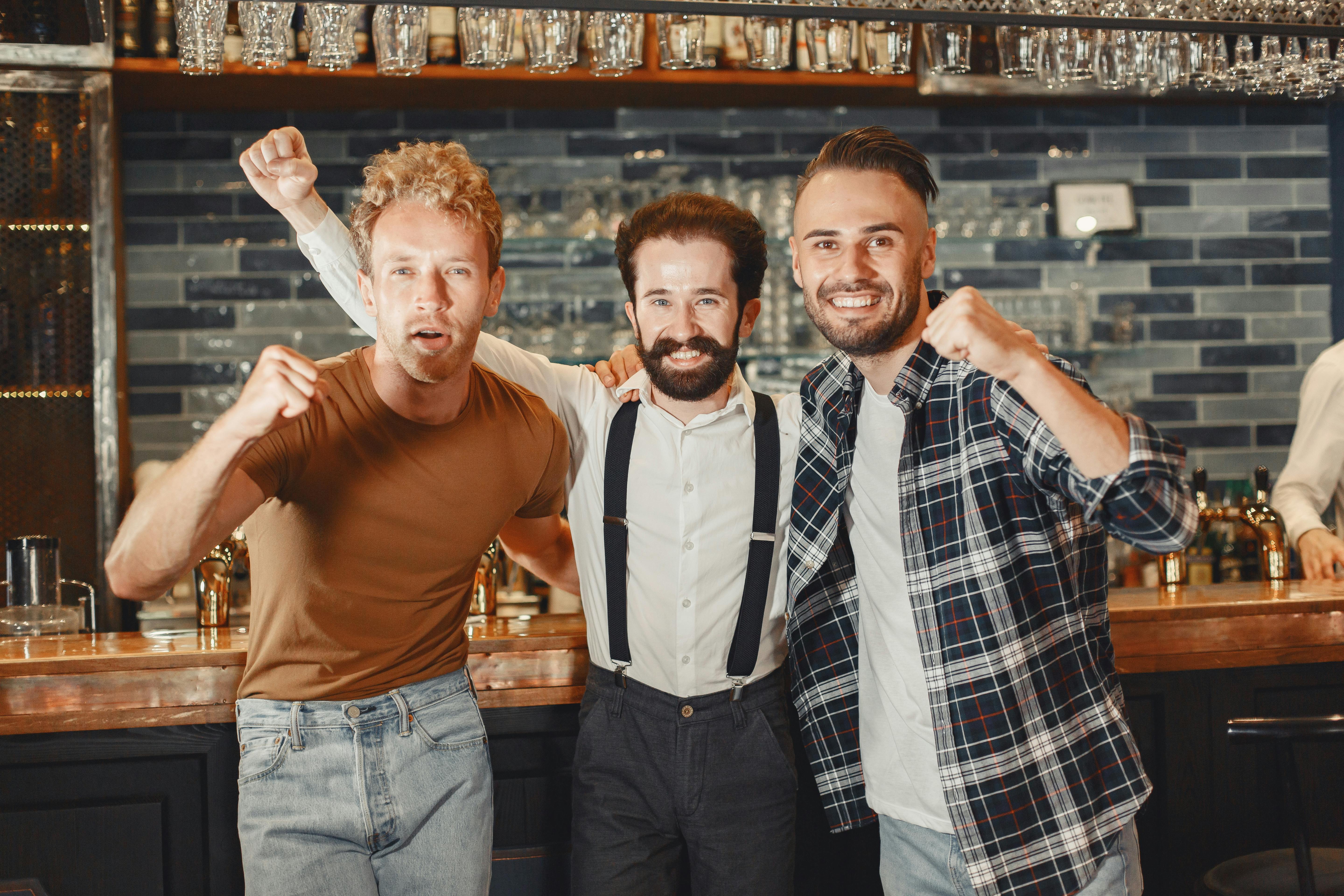 Three happy friends embrace and celebrate in a stylish indoor bar setting.