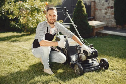 Man in Black and White Plaid Long Sleeve Shirt Sitting beside a Lawn Mower