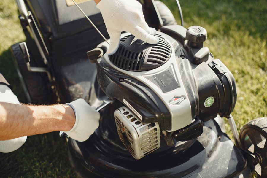 Hands in gloves adjusting a lawn mower outdoors, perfect for gardening themes.