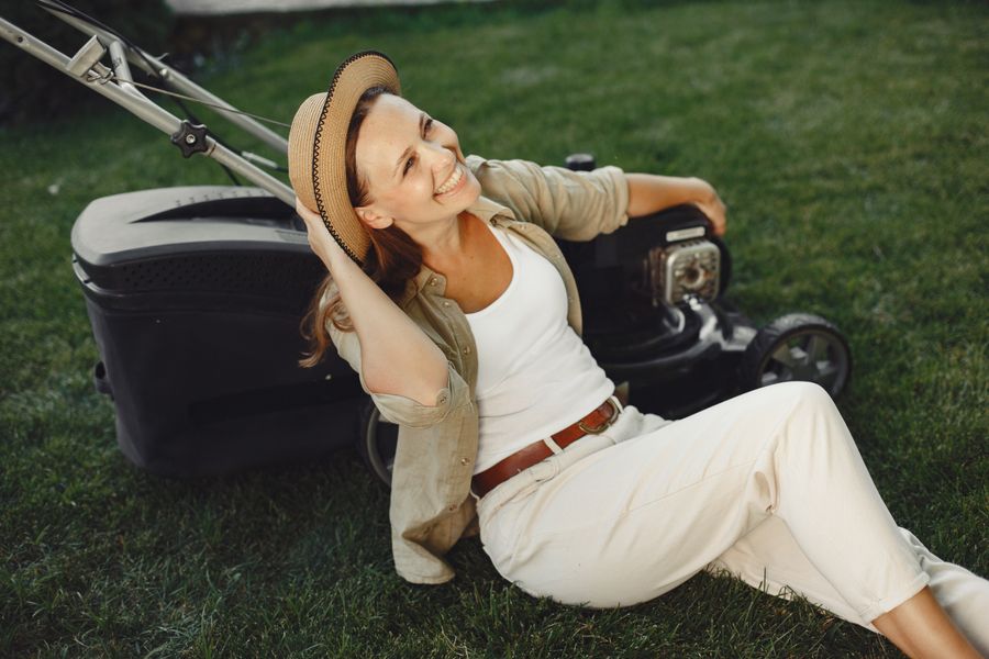 A cheerful woman relaxes on a lawn with a mower, exuding a serene and content vibe.
