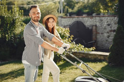 Free Smiling couple enjoys gardening together, using lawn mower in sunny outdoor garden. Stock Photo