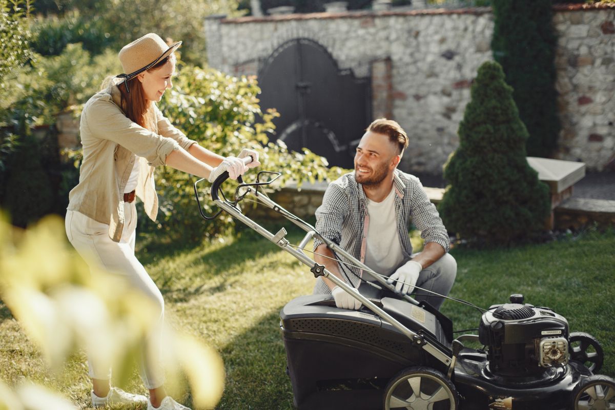 A cheerful couple working together in a garden with a lawn mower.
