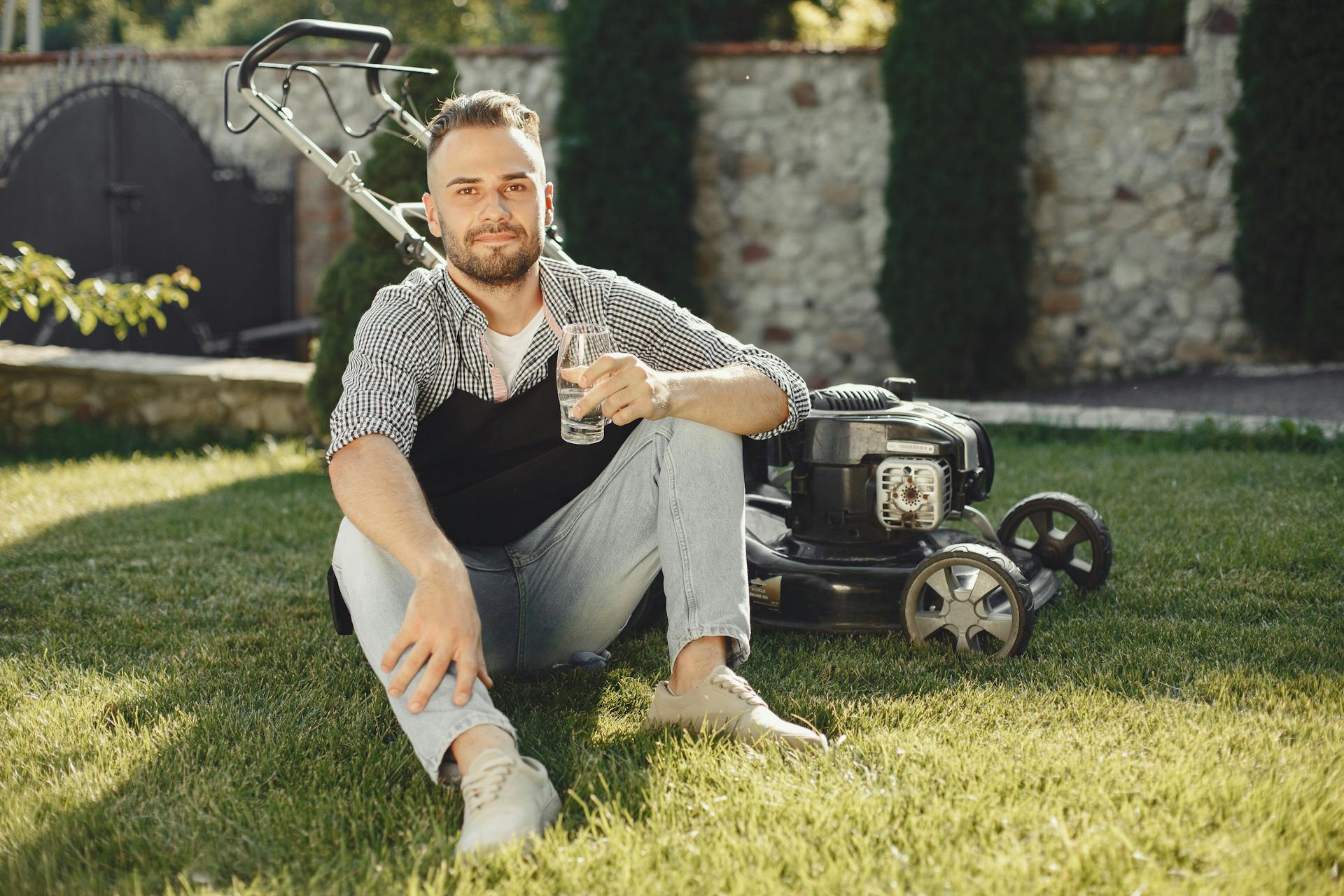 Man in Black and White Checkered Shirt Holding Clear Drinking Glass while Sitting on Green Grass Field