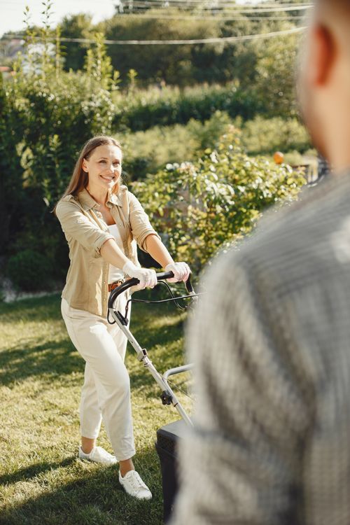 Free Smiling woman mowing the lawn in a sunny backyard garden. Stock Photo