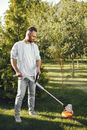 Man in White Long Sleeve Shirt Holding White and Orange Grass Cutter