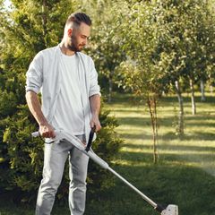 A man holding a light electric grass trimmer in a garden