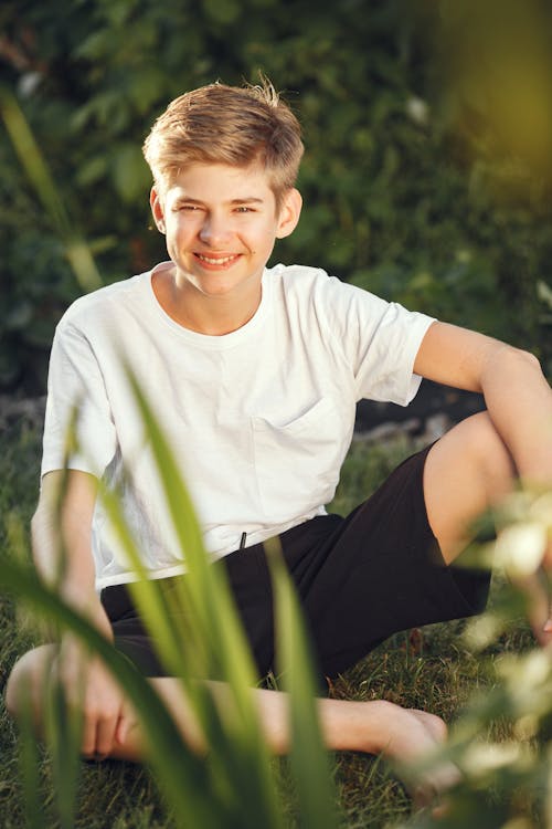 Free Boy in White Crew Neck T-shirt and Black Shorts Sitting on Green Grass Stock Photo